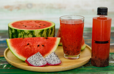 Close up studio shot of sweet delicious healthy sliced watermelon and fresh ripe cold dragon fruit juice in glass placed on wood plate and no brand bottle packaging for advertisement with copy space