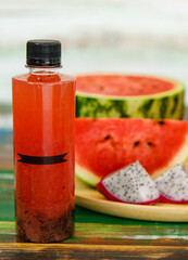 Close up studio shot of sweet delicious healthy sliced watermelon and fresh ripe cold dragon fruit juice in glass placed on wood plate and no brand bottle packaging for advertisement with copy space