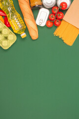 Vertical image with groceries, food donations on green background with copy space - pasta, vegatables, canned food, baguette, cooking oil, tomatoes. Food bank, food delivery concept