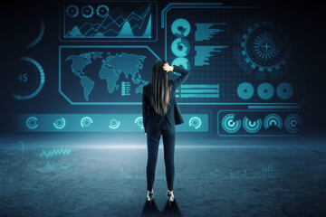 Back view of attractive young european business woman standing on dark background with glowing digital hud business interface. Future, technology and innovation concept.