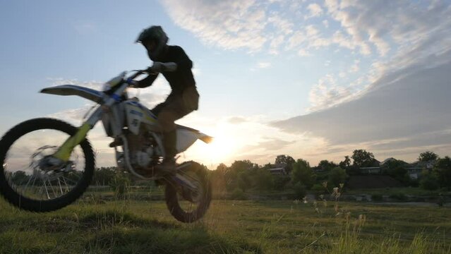 sport man in sportswear and helmet jumping on grass hills on enduro bike motorcycle cross country in slow motion on sunset in rural area
