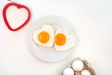 Romantic breakfast. Heart shaped fried eggs on a plate. white background, flat lay, copy space. Valentines day breakfast idea.