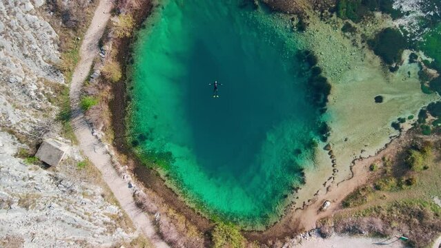 A rising aerial shot showing a diver floating on his back in the middle of the Izvor Cetine natural karst spring, a blue-green natural beauty that's a famous travel attraction in rural Croatia.