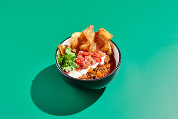 Chili con carne on colour background with hard shadow. Mexican chili in minimal style on green table. Traditional mexican cuisine on trendy design. Chili soup in bowl contemporary concept.