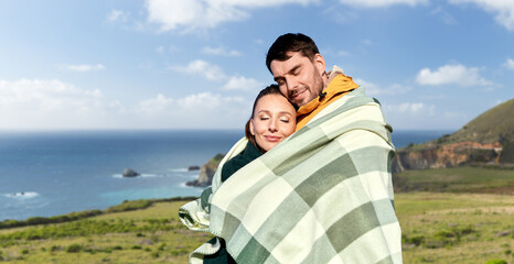 love, travel and tourism concept - happy smiling couple in warm blanket over big sur coast of california background