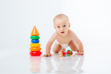 a little baby boy in a diaper crawls on a white background playing a multi-colored pyramid , studio shooting