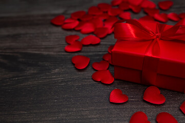 A red box with a gift in small red hearts on a wood background, a template for Valentines day with a copy space, a postcard for February 14 with a place for text.