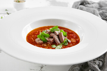 Authentic georgian beef soup Kharcho. Georgian lamb and rice soup. Caucasian dish - kharcho soup with rice, beef and coriander leaves. Kharcho in white plate on stone table.