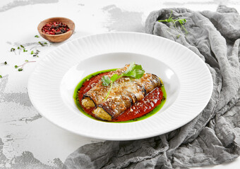 Eggplant rolls stuffed with tomato and cheese. Baked eggplant and cheese rollatini. Eggplant appetizer in white plate on stone background. Plant-based menu.