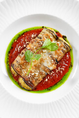 Eggplant rolls stuffed with tomato and cheese. Baked eggplant and cheese rollatini. Eggplant appetizer in white plate on stone background. Plant-based menu.