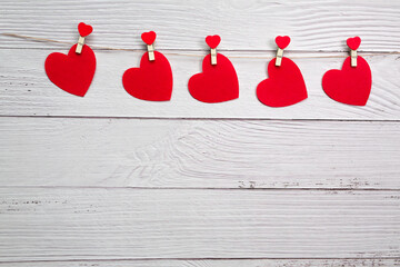 Red hearts hanging on a rope with clothespins on a wood background with a garland. Valentines Day.