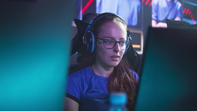 Concentrated young female gamer playing video game on computer then exhaling in relief after winning match during professional esports championship