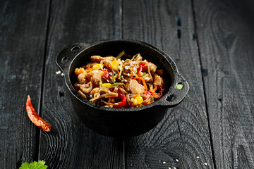 Yakisoba noodle with chicken and vegetables on wooden background. Japanese stir fry noodles in wok on black table with ingredients. Chicken with buckwheat soba on wok. Oriental cuisine. Wok menu.