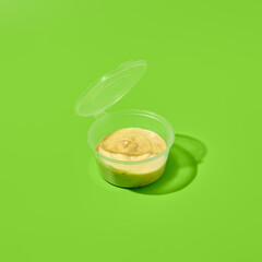 Sauce in plastic container on green background. Sauce package in minimal style. Takeaway food. Fast...