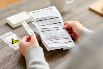 medicine, self testing and pandemic concept - hands of woman reading coronavirus test manual at home