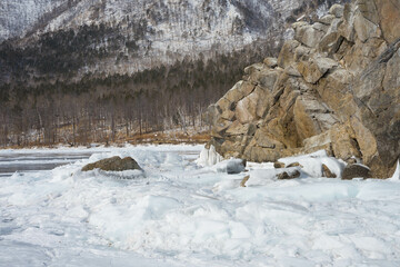 Fototapeta na wymiar frozen lake with ice against the background of rocks and sky