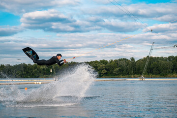 Experienced male wakeboarder performing jump over water holding on towing cable