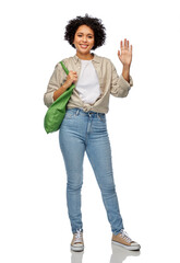 Fototapeta premium eco living, zero waste and sustainability concept - portrait of happy smiling woman with green reusable canvas bag for food shopping waving hand over white background
