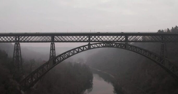 Sliding aerial shot of San Michele iron bridge on Adda River on a foggy winter morning.