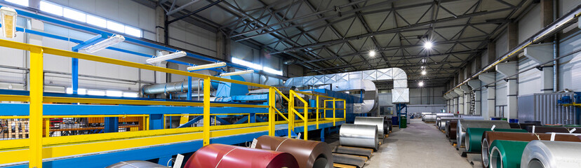 Panoramic photo shot of roll of painted galvanized steel sheet at cutting machine, ironworks and metalwork in factory. Plant concept