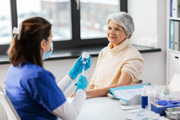 medicine, health and vaccination concept - doctor or nurse filling syringe with vaccine or drug and senior woman at hospital