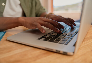 Young adult black male typing on laptop. Close up of hands, working from home, sitting at modern styled kitchen counter.
