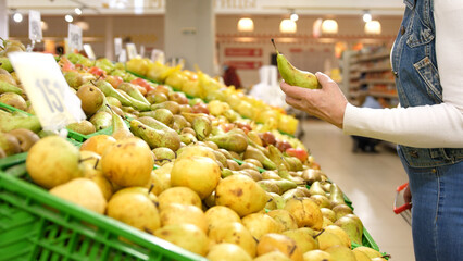 Elderly woman chooses ripe organic pears in the supermarket. Woman picks ripe organic pears in the supermarket during quarantine.