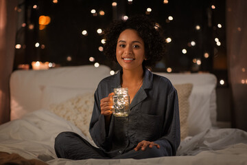 people, bedtime and rest concept - happy smiling woman in pajamas sitting in bed at night