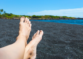 Woman's feet relaxing on black sand Beach in Hawaii