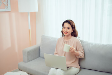 Obraz na płótnie Canvas woman at remote work on a sofa near table with a laptop holding a mug