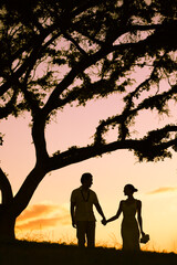 Silhouette of happy just married couple holding hand walking in the sunset 