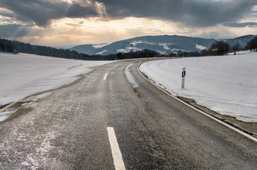 Frozen road danger safety, with plenty of snow around during dawn with sunset and mountain range in...