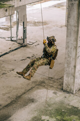 Special forces operator rappeling down the abandoned building on the rope. Multicam camo with coyote brown addons.