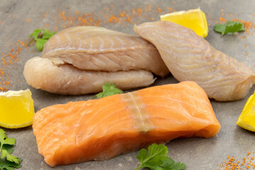 salmon steak and raw coalfish fillet on a gray background with lemons