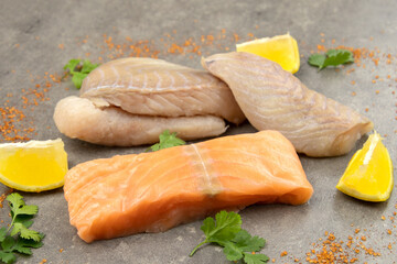 salmon steak and raw coalfish fillet on a gray background with lemons