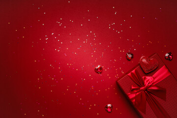 Valentine's Day gift in a red box tied with a red ribbon and red crystals, heart-shaped rubies, rhinestones, glitter on a red background.