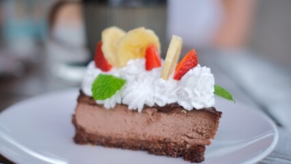 Tempting sliced piece of chocolate cake decorated with cream, strawberries and banana, sweet food in cafe
