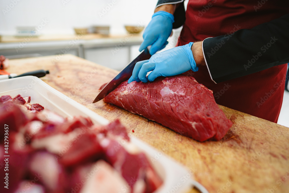 Wall mural Butcher cutting slices of raw meat on wooden board