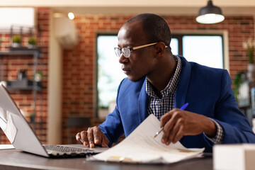 Company employee analyzing documents on clipboard to plan business strategy with laptop....