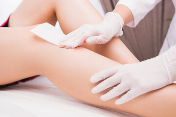 Woman with long perfect legs and smooth skin having wax stripe depilation hair removal procedure on legs in beauty salon.