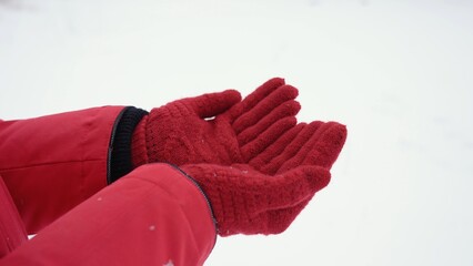 Closeup view stock photo of two female hands in red gloves isolated on white snow background. Woman holding both empty palms making cupped gesture with her outstretched arms 