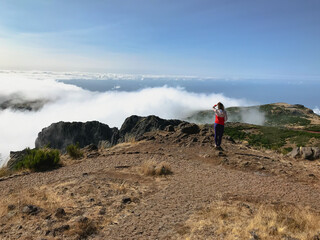 Person in sports wear standing high in the mountains looking at clouds in windy weather.