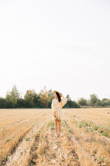 Naklejka na ściany i meble Young beautiful brunette on a summer day. girl in yellow dress. Large straw hat with a bouquet of wheat. Agricultural texture