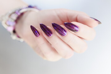 Female hand with long nails and purple plum manicure holds a bottle of nail polish