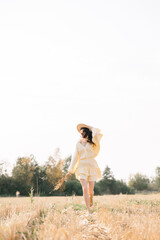 Caucasian young brunette walking through a wheat field. girl in yellow summer dress and straw hat. sheared golden ears of wheat, rye. Close-up portrait of a beautiful girl with brown eyes. 