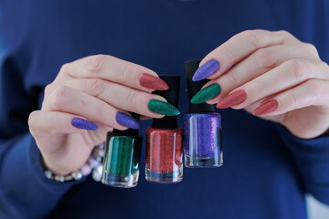 Woman's hands with long nails and multi-colored manicure, bottles of nail polishes