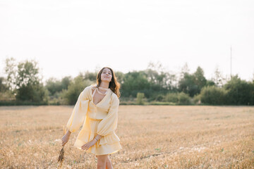 Caucasian young brunette walking through a wheat field. girl in yellow summer dress and straw hat. sheared golden ears of wheat, rye. Close-up portrait of a beautiful girl with brown eyes. 