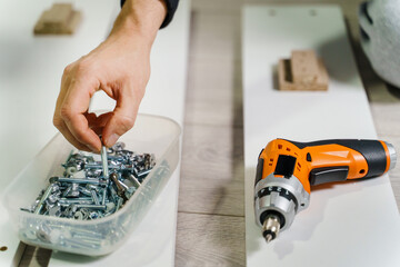 Close up on midsection of unknown caucasian man holding electric screwdriver while putting together Self assembly furniture of plywood screwing screws following instructions - DIY concept copy space - Powered by Adobe