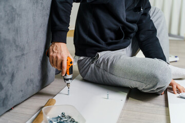 Close up on midsection of unknown caucasian man holding electric screwdriver while putting together...