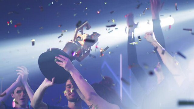 Excited gamer woman professional esportsman winner raising golden cup over head while celebrating victory in gaming tournament with male teammates